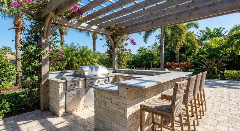 Stone outdoor kitchen with grill island and pergola in a Florida backyard