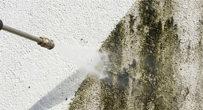 Pressure washer cleaning mildew-stained stucco siding